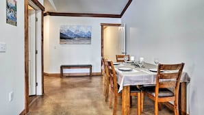 A dining area with a wooden table set for four, a bench, and a mountain landscape painting on the wall.