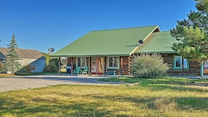 A log cabin with a green metal roof, a porch with green chairs, and a gravel driveway.