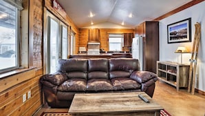 A cozy cabin interior with a leather sofa, a wooden coffee table, and a kitchen area in the background.