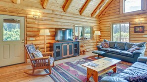 A log cabin interior with a wooden ceiling, a large flat-screen TV, a leather sofa, a rocking chair, and a patterned rug. - 13 Mi to Mt Shasta: Log Home on 60 Acres! (McCloud)