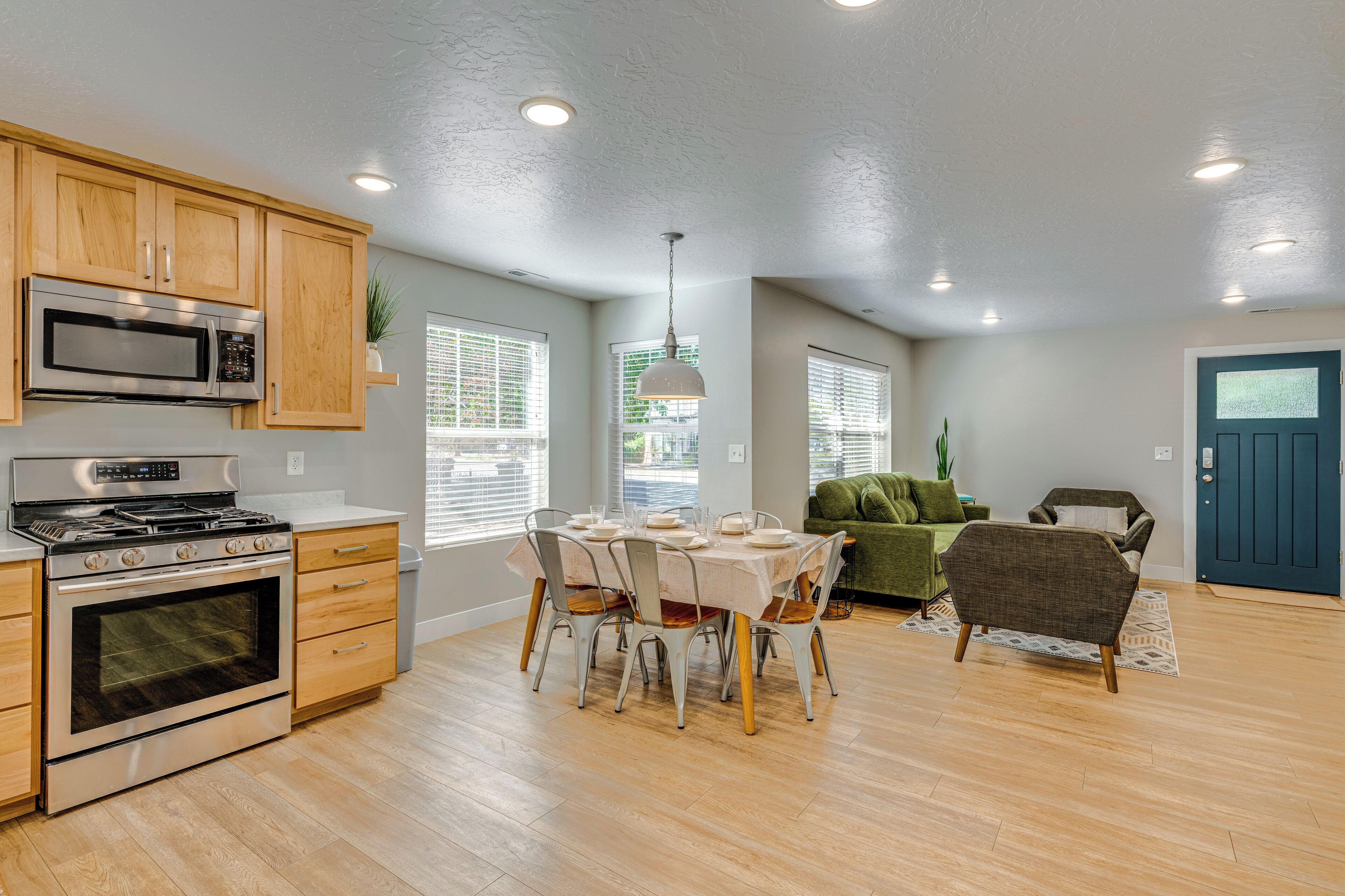 A modern kitchen with wooden cabinets, a stainless steel stove, and a dining area with a table and chairs.