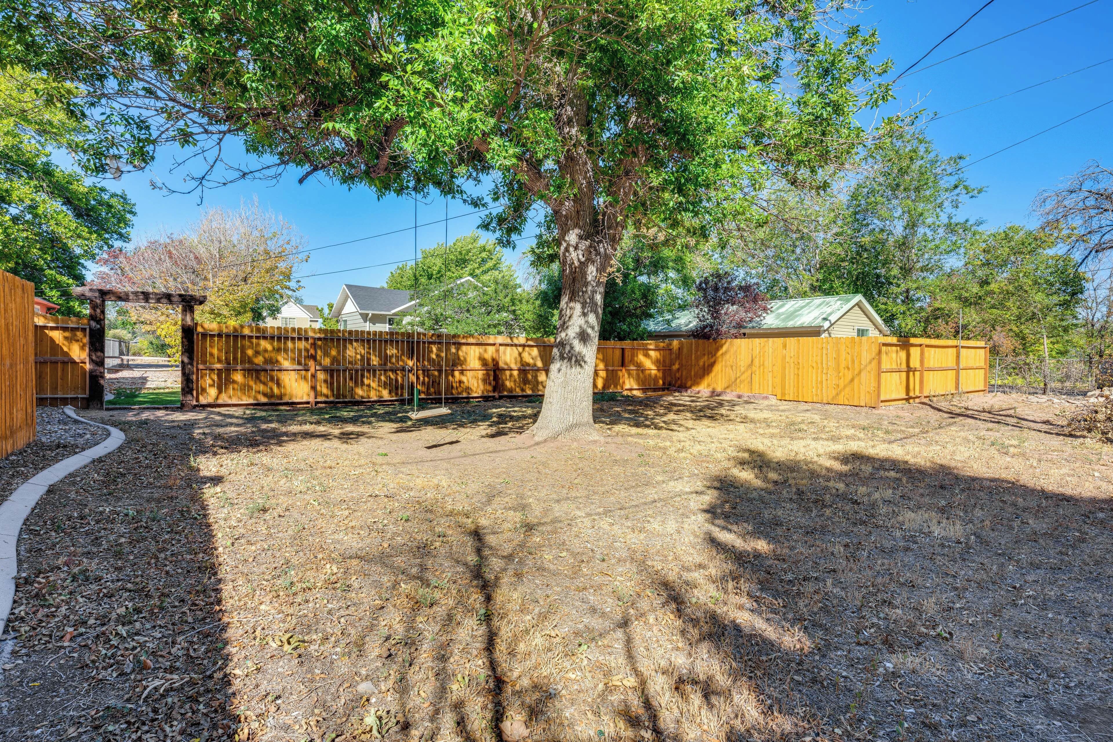 A fenced backyard with a wooden structure, a tree, and a house in the background.