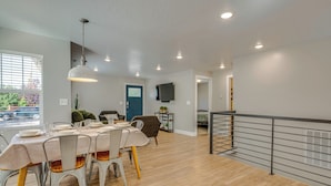 Un coin repas avec une table dressée pour quatre personnes, un téléviseur fixé au mur et un escalier doté d’une rampe en métal.