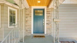 Une porte d’entrée avec une porte bleue, une boîte aux lettres blanche et un paillasson sur lequel est écrit « Bonjour ».
