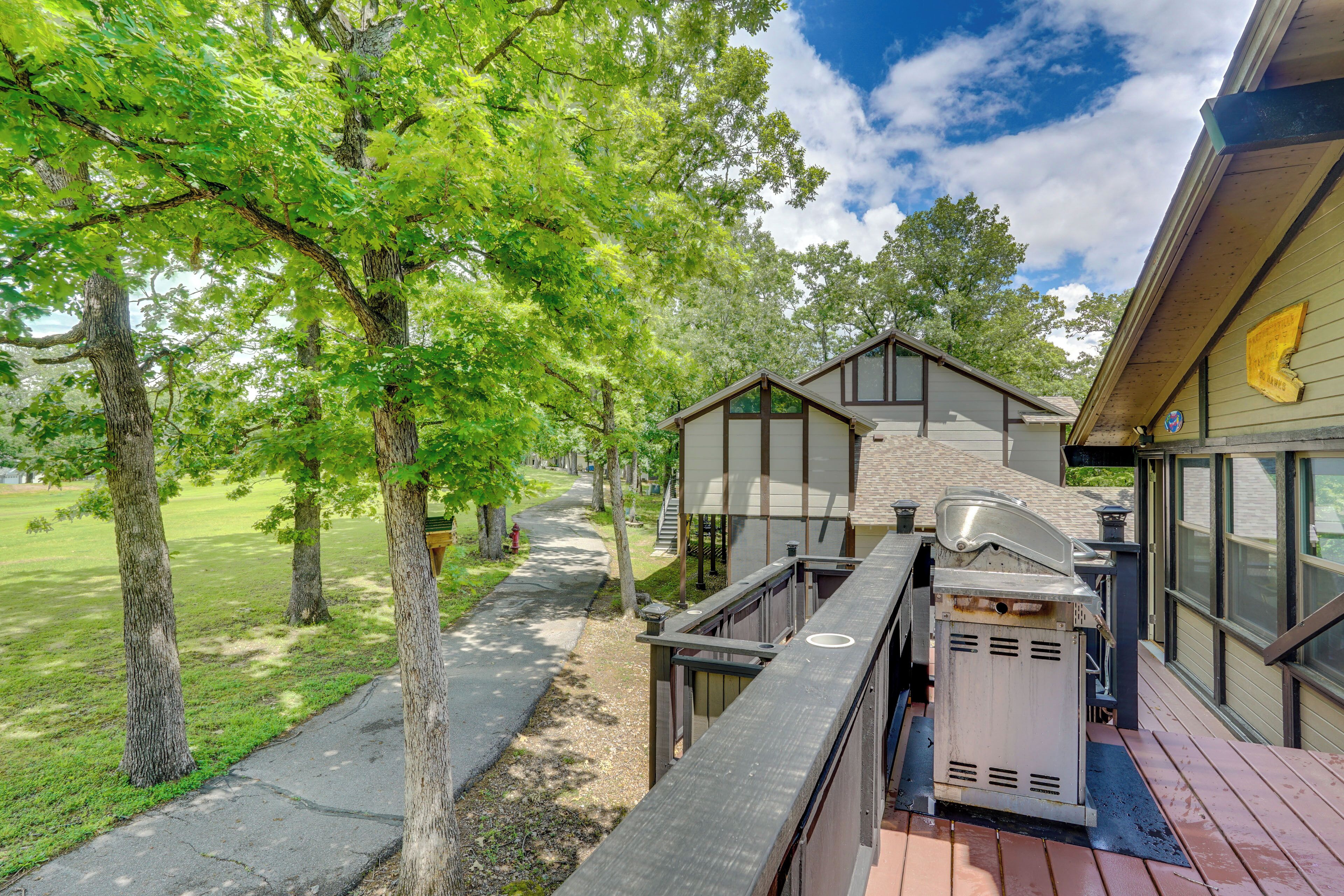 A deck with a grill, a pathway, and a building with large windows and a stone facade.