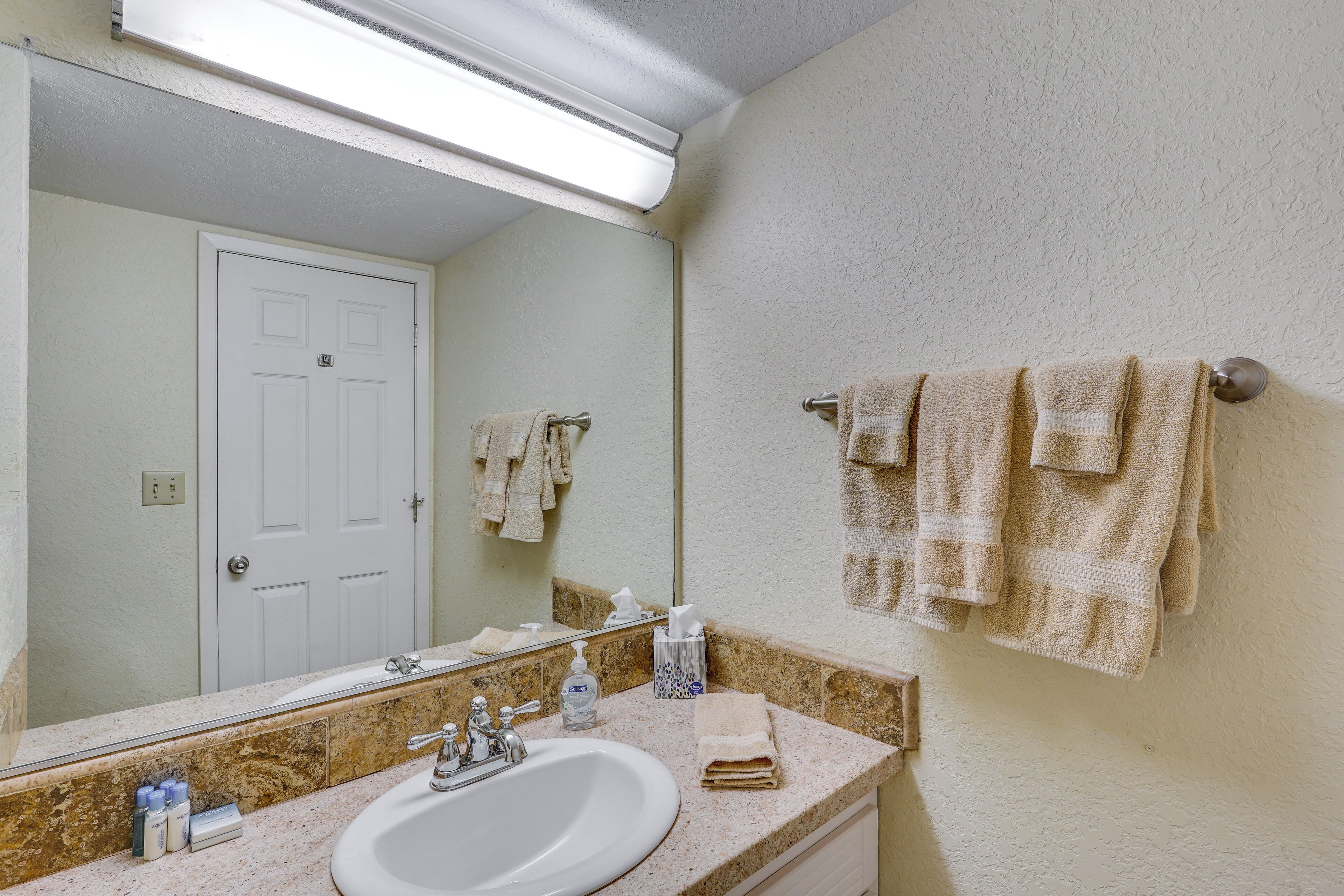 Un baño con lavamanos blanco, espejo y toallero.