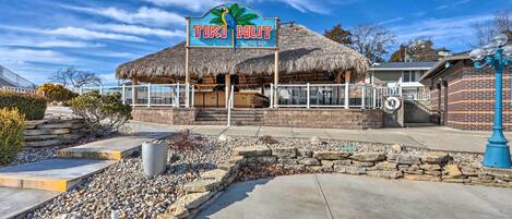 Un petit chalet de style tiki avec une enseigne indiquant « TIKI HUT POOL BAR » et un toit de chaume.