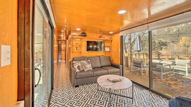Ein gemütliches Interieur mit einer Couch, einem runden Tisch und einem großen Fenster mit Blick ins Freie.