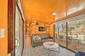 A cozy interior with a sofa, a round table, and a large window offering a view of the outdoors.