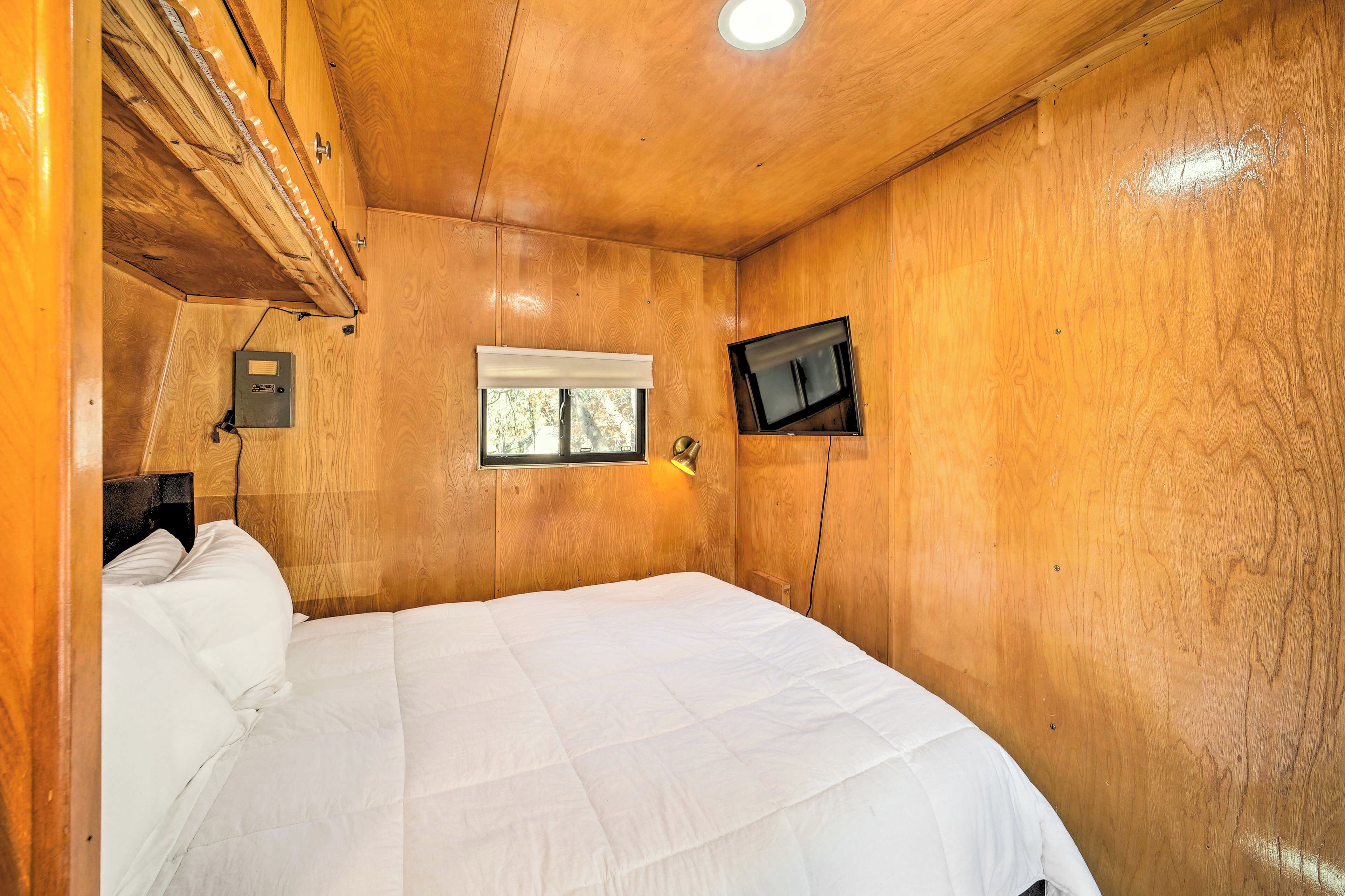 A wooden-paneled bedroom with a bed, a window, and a mounted television.