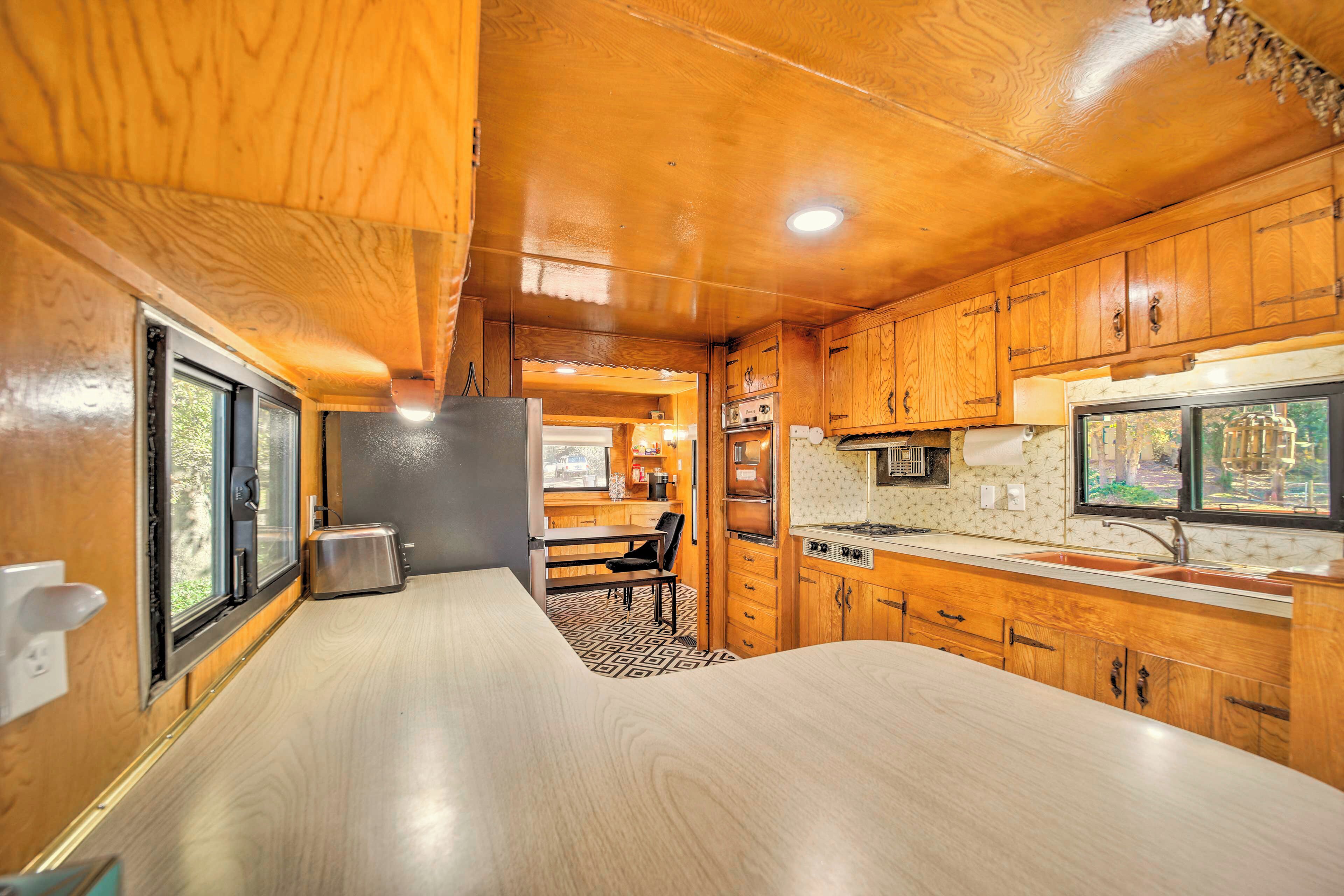 A compact kitchen with wooden cabinets, a central island, and a window overlooking a garden.