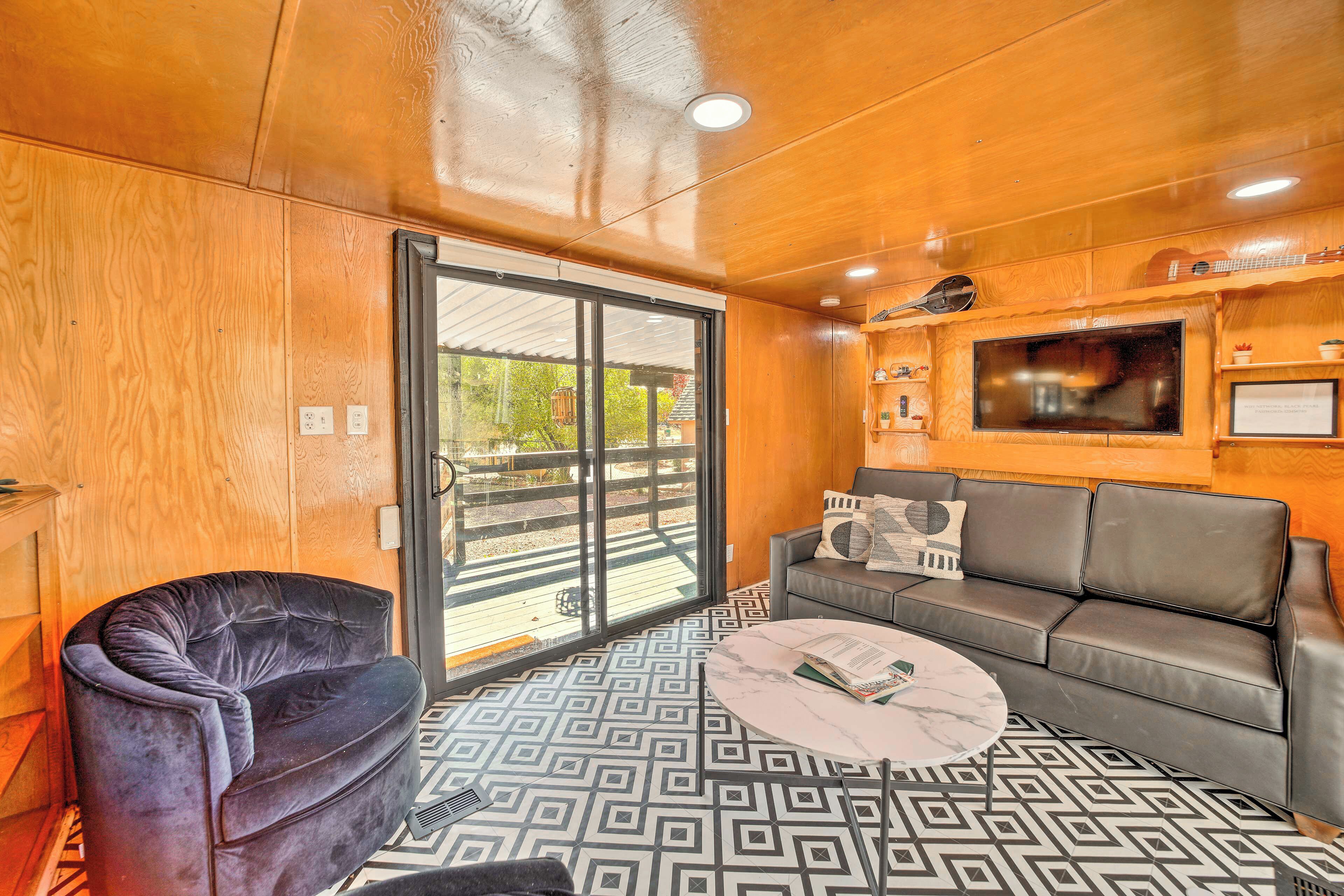 A modern living room with a black leather sofa, a patterned floor, and a large window with a view of the outdoors.