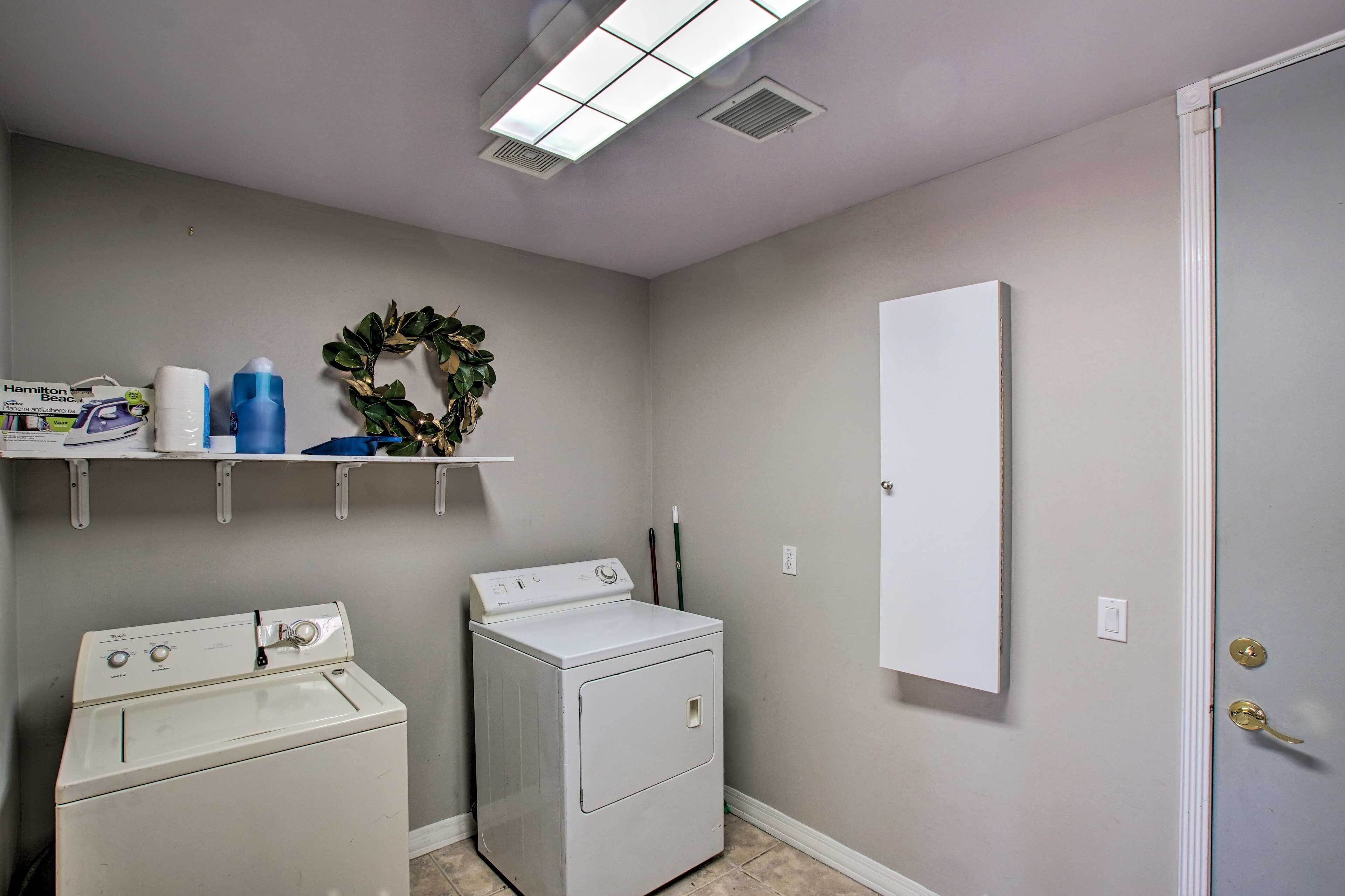 A laundry room with two washing machines, a shelf with cleaning supplies, a decorative wreath, and a door with a mirror.