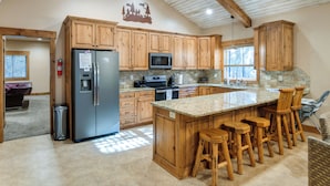 A spacious kitchen with wooden cabinets, a granite countertop, and a large island with bar stools. - Outdoor Adventure Hub ~ 20 Miles to Yellowstone! (Island Park)