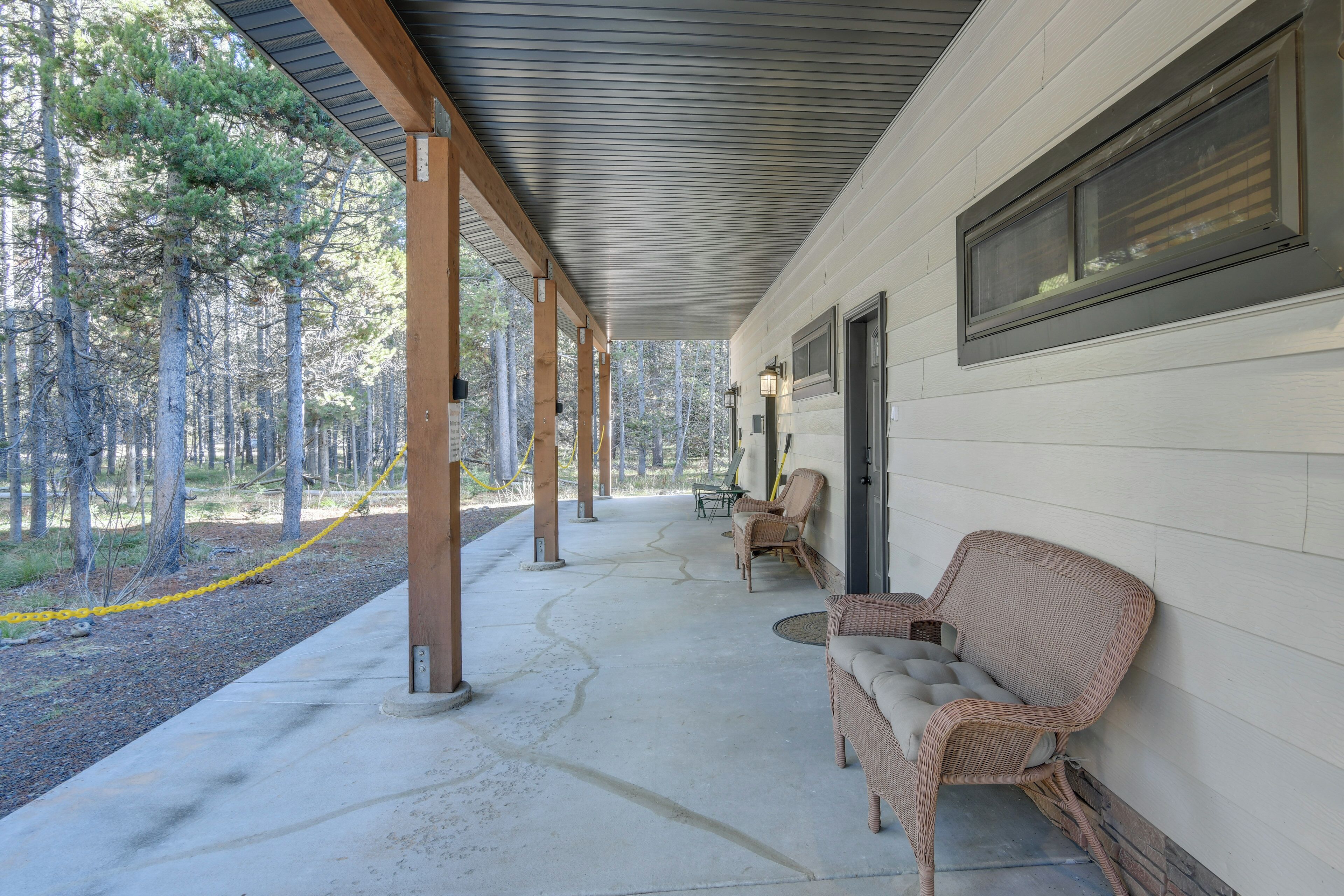 A covered porch with wicker furniture and a view of a forest.