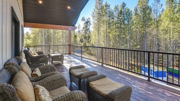 A covered deck with wicker furniture and a view of a forest. - Outdoor Adventure Hub ~ 20 Miles to Yellowstone! (Island Park)