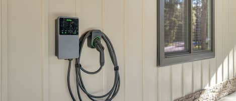 A wall-mounted electric vehicle charging station with a cable connected to it, near a window with a stone base.