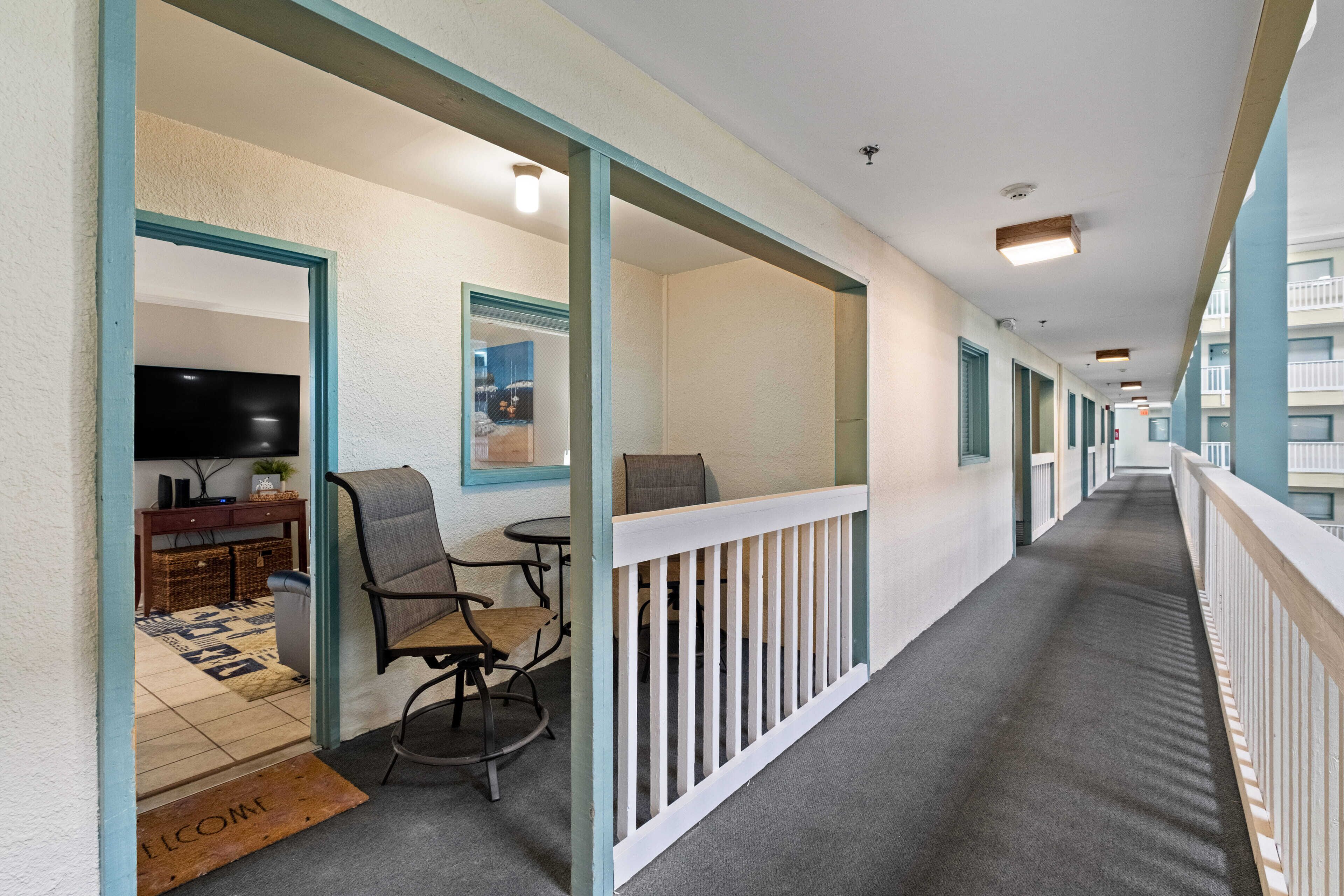 A corridor with a dining area featuring a table and chairs, a television, and a welcome mat.