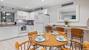 A modern kitchen with white cabinets, a microwave, and a refrigerator. There is a dining table with chairs and a sign that reads "Welcome". - Steps to Pool & Beach: Family Condo in Hilton Head (Hilton Head Island)