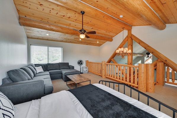 A spacious living area with a large sectional sofa, a bed, and a wooden staircase. - Stunning 3-story Mountain View Getaway in Payson (Payson)
