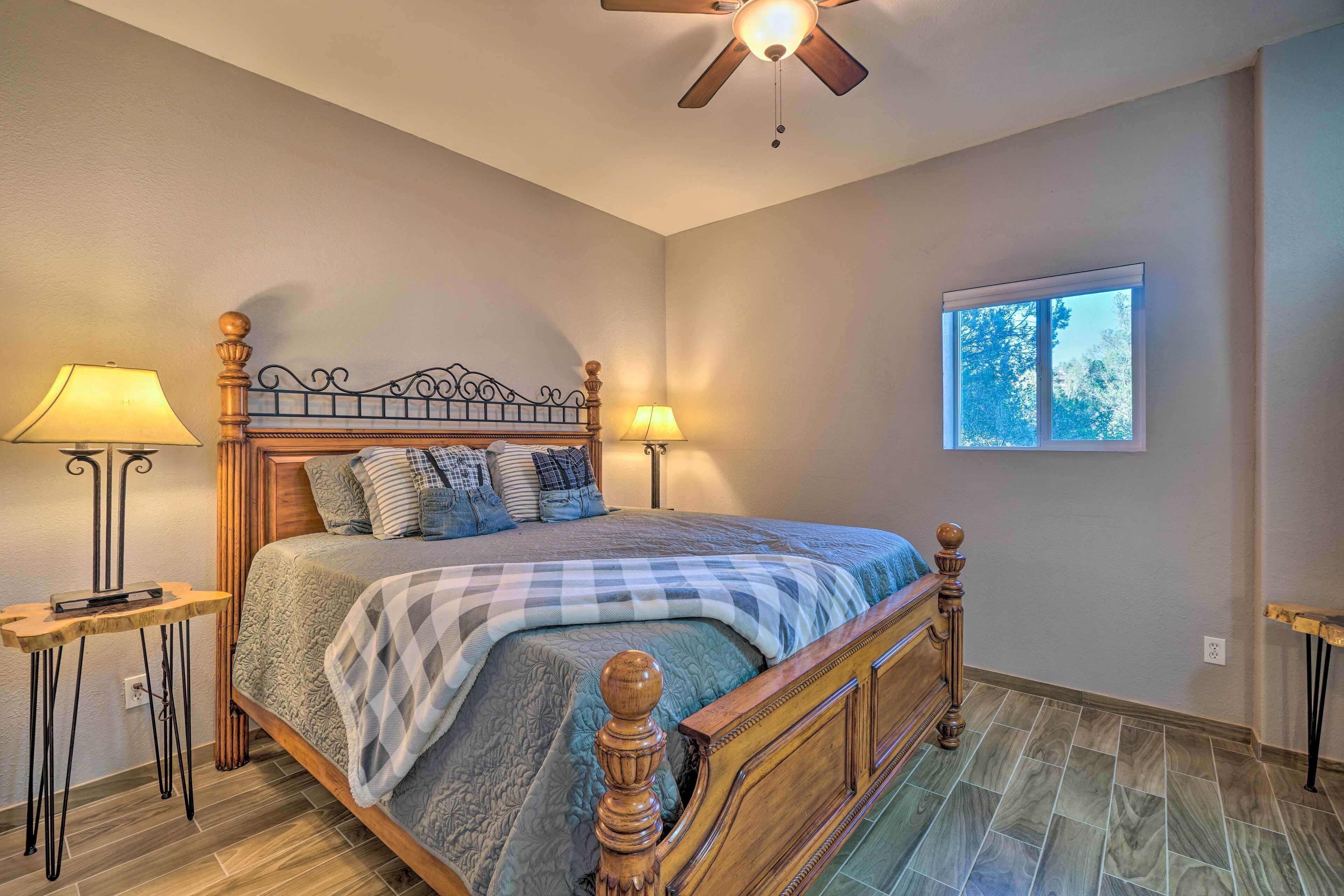 A bedroom with a wooden bed, two bedside lamps, a ceiling fan, and a window with a view of trees.