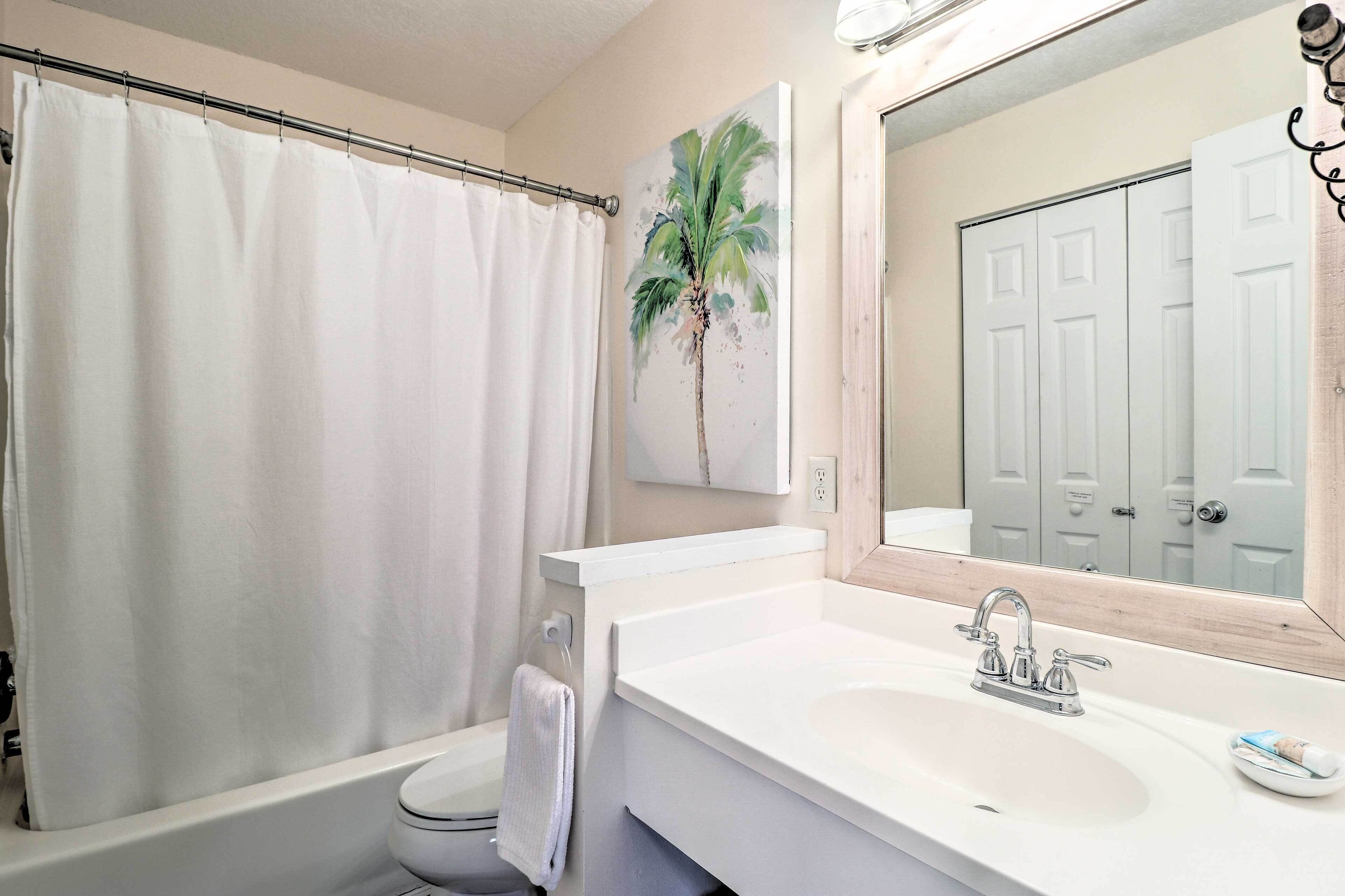 A bathroom with a shower curtain, a sink with a mirror, and a toilet.