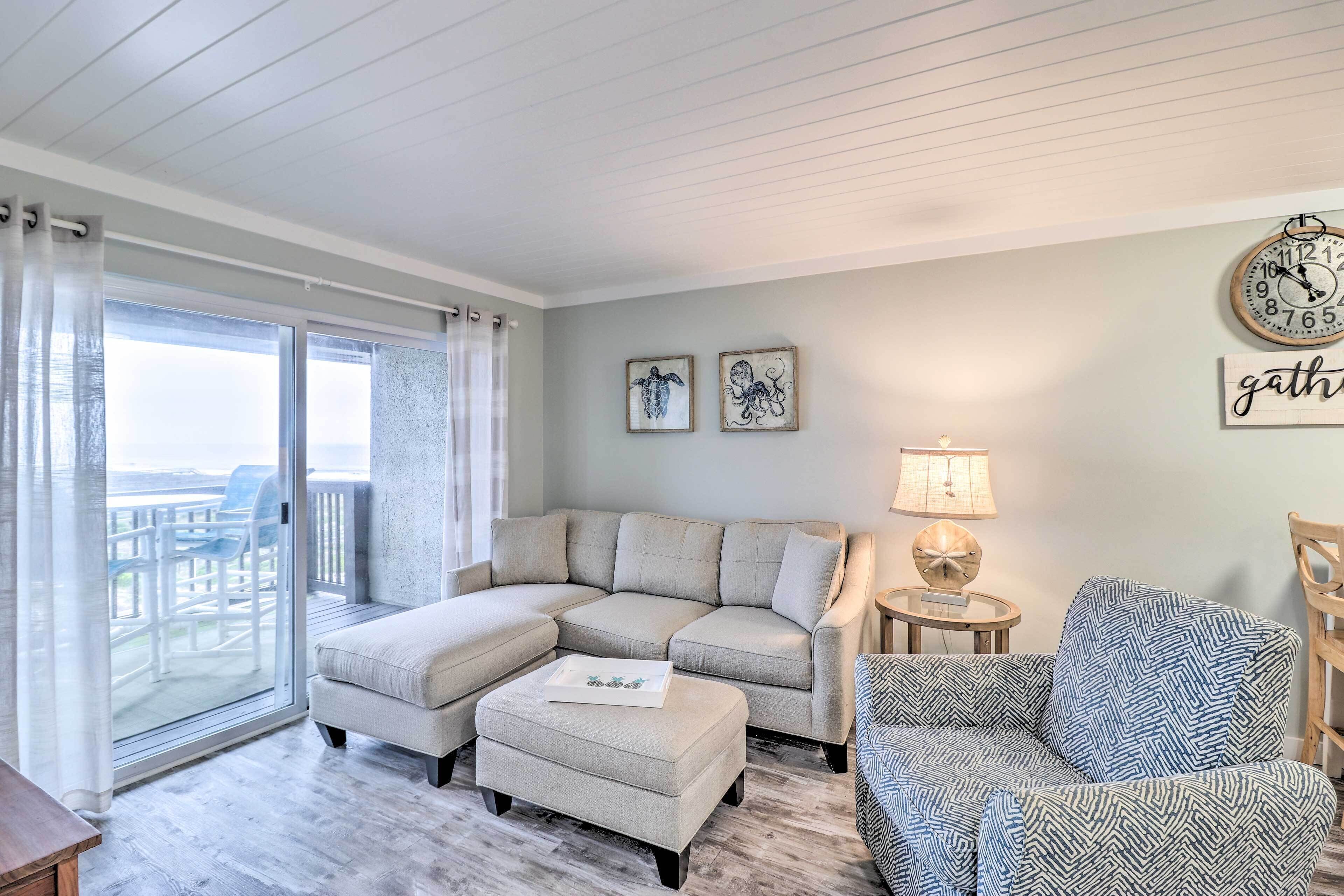 A living room with a sectional sofa, a patterned armchair, a small side table, and a view through a sliding glass door to an outdoor deck.