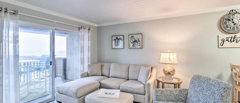 Una sala de estar con un sofá modular, un sillón estampado, una mesita auxiliar y vistas a una terraza exterior a través de una puerta corrediza de vidrio.