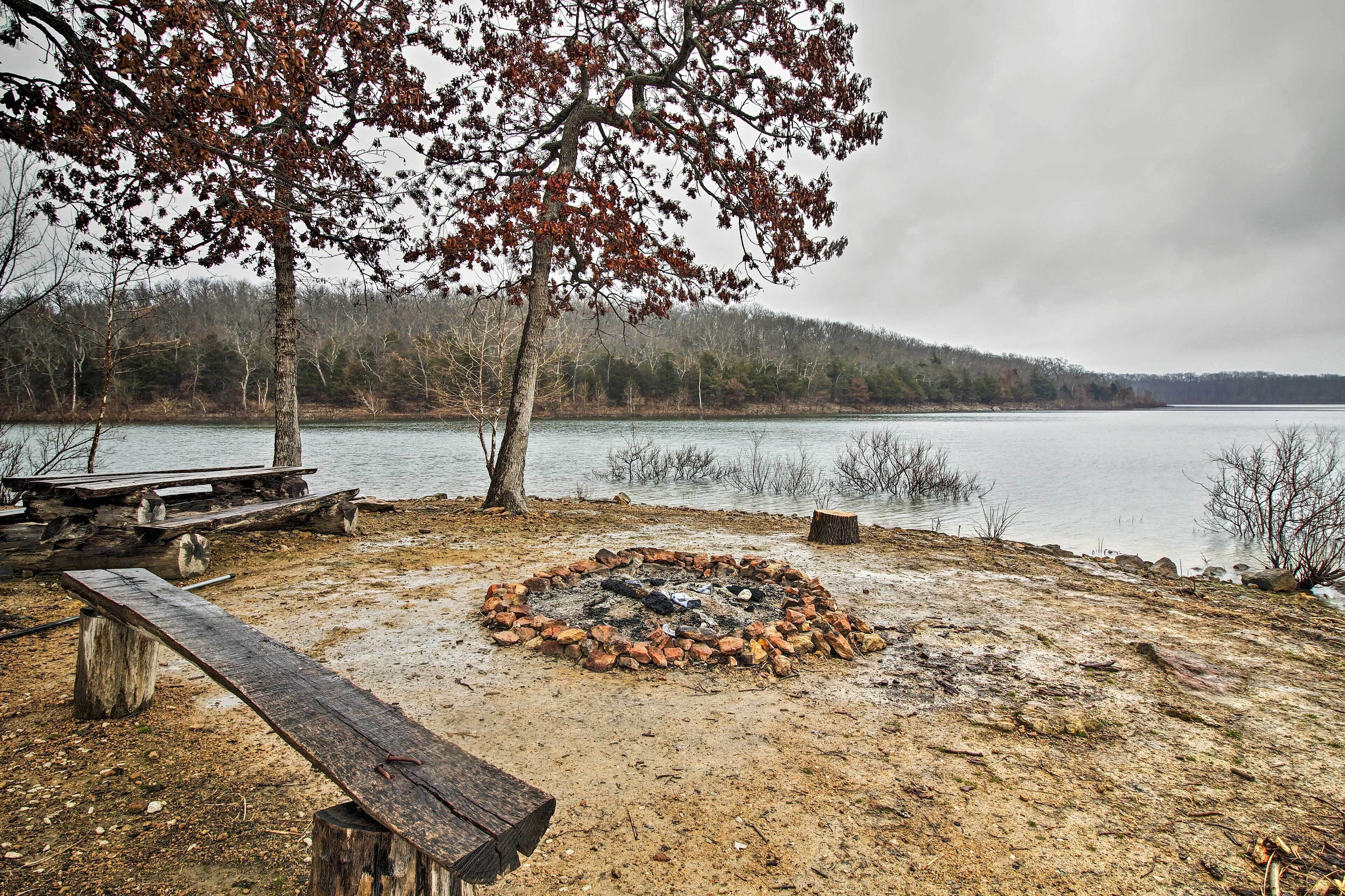 A lakeside campsite with a fire pit, picnic table, and benches.