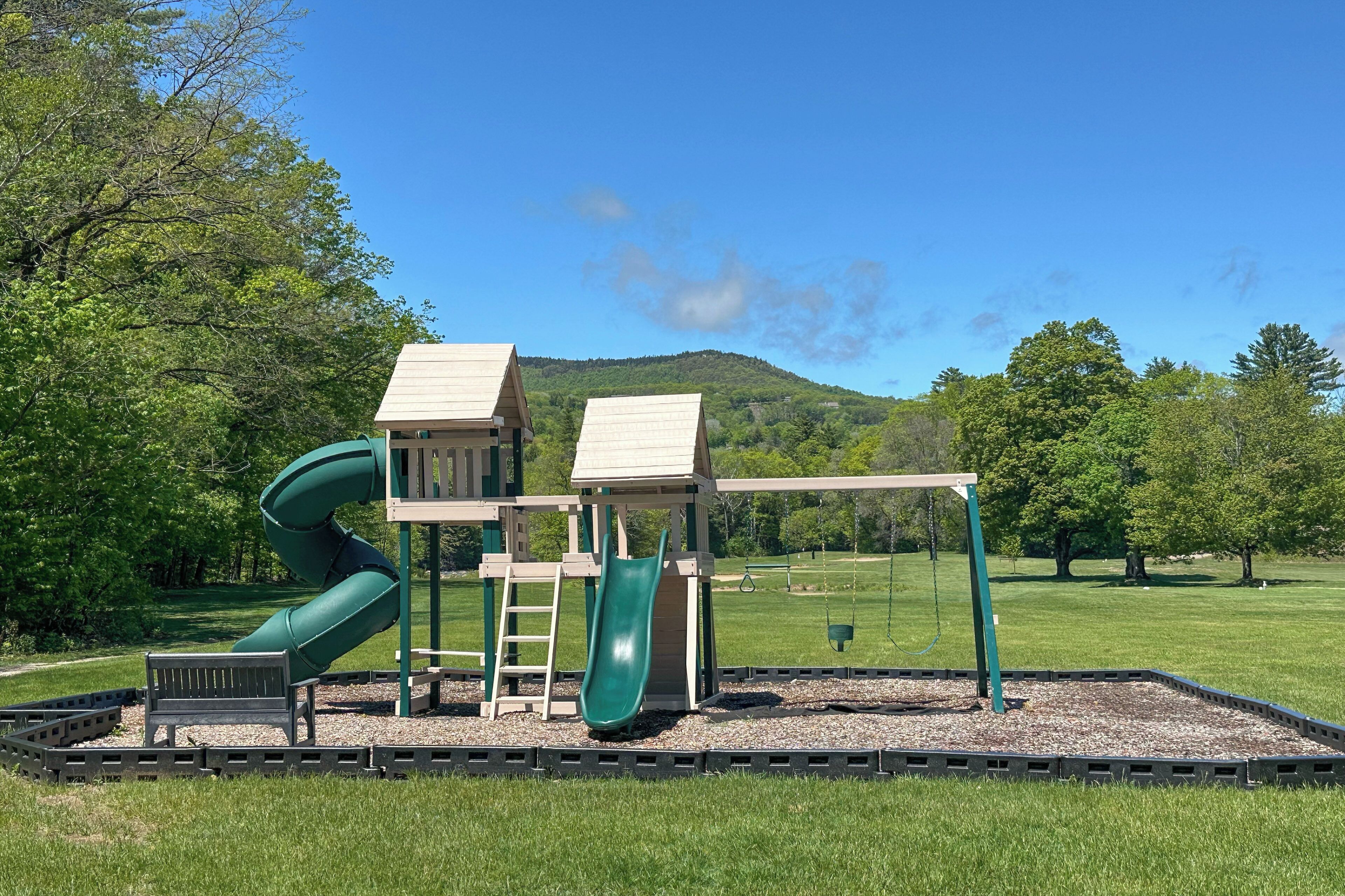 A playground with a slide, a swing set, and a small building structure.