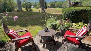 A patio with two Adirondack chairs, a small round table, and a hanging planter. - Glen Condo w/ Mountain Views: Walk to Story Land (Glen)