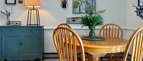 A dining area with a wooden table and chairs, a teal cabinet, a lamp, and wall art.