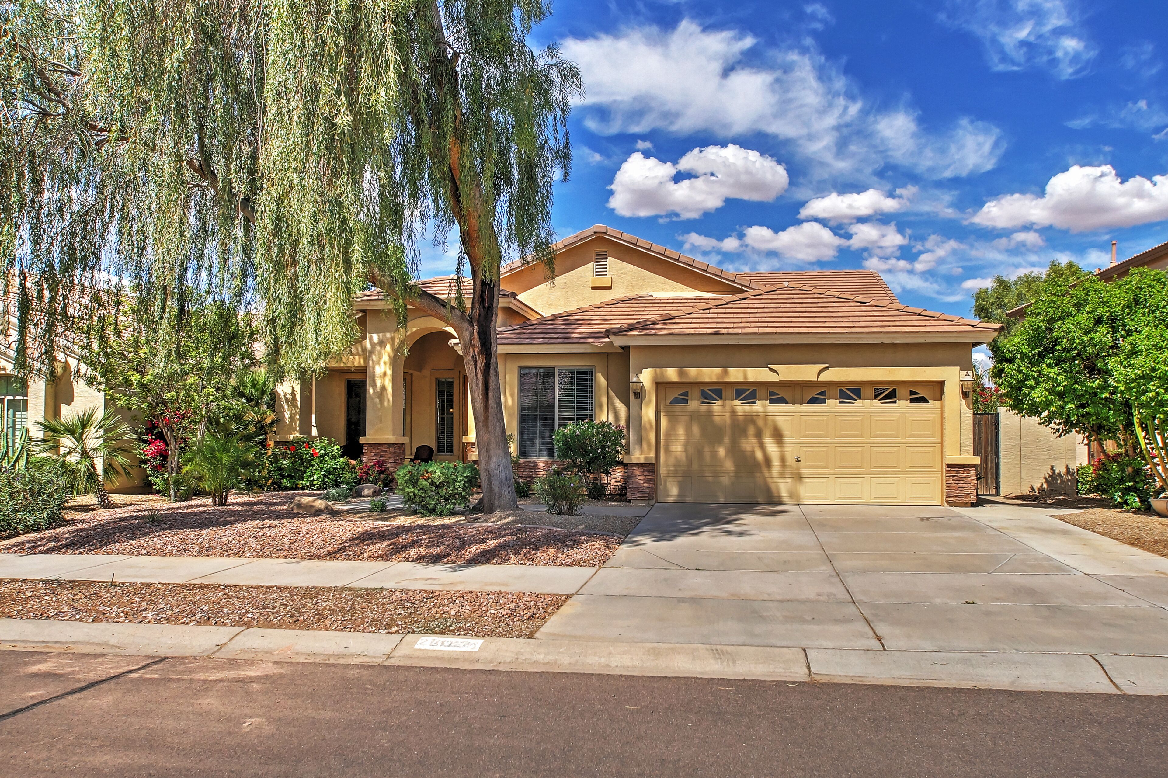A single-story house with a garage, a driveway, and a well-maintained garden with various plants and a tree.