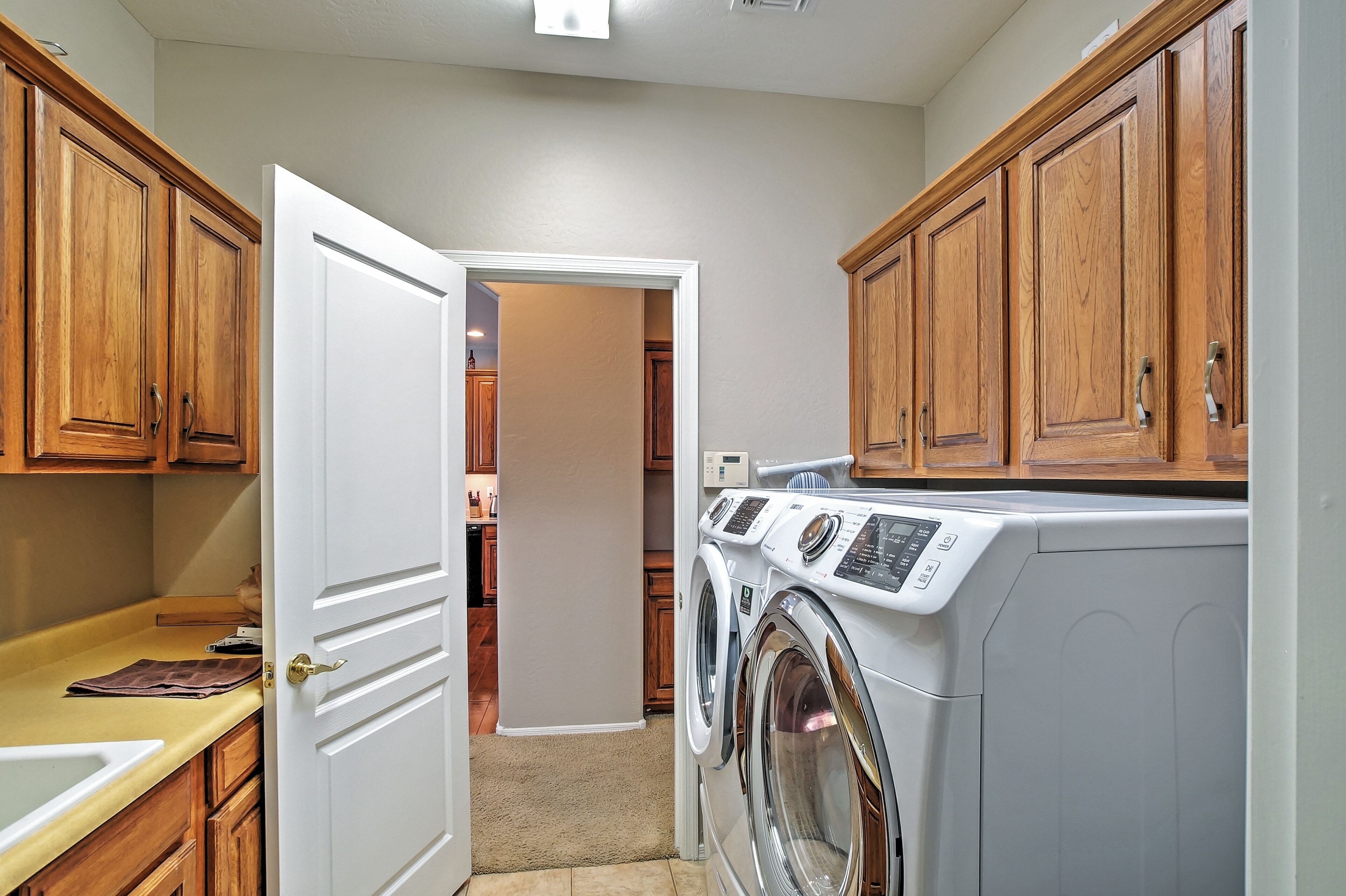 A laundry room with wooden cabinets, a washing machine, and a door leading to a hallway.