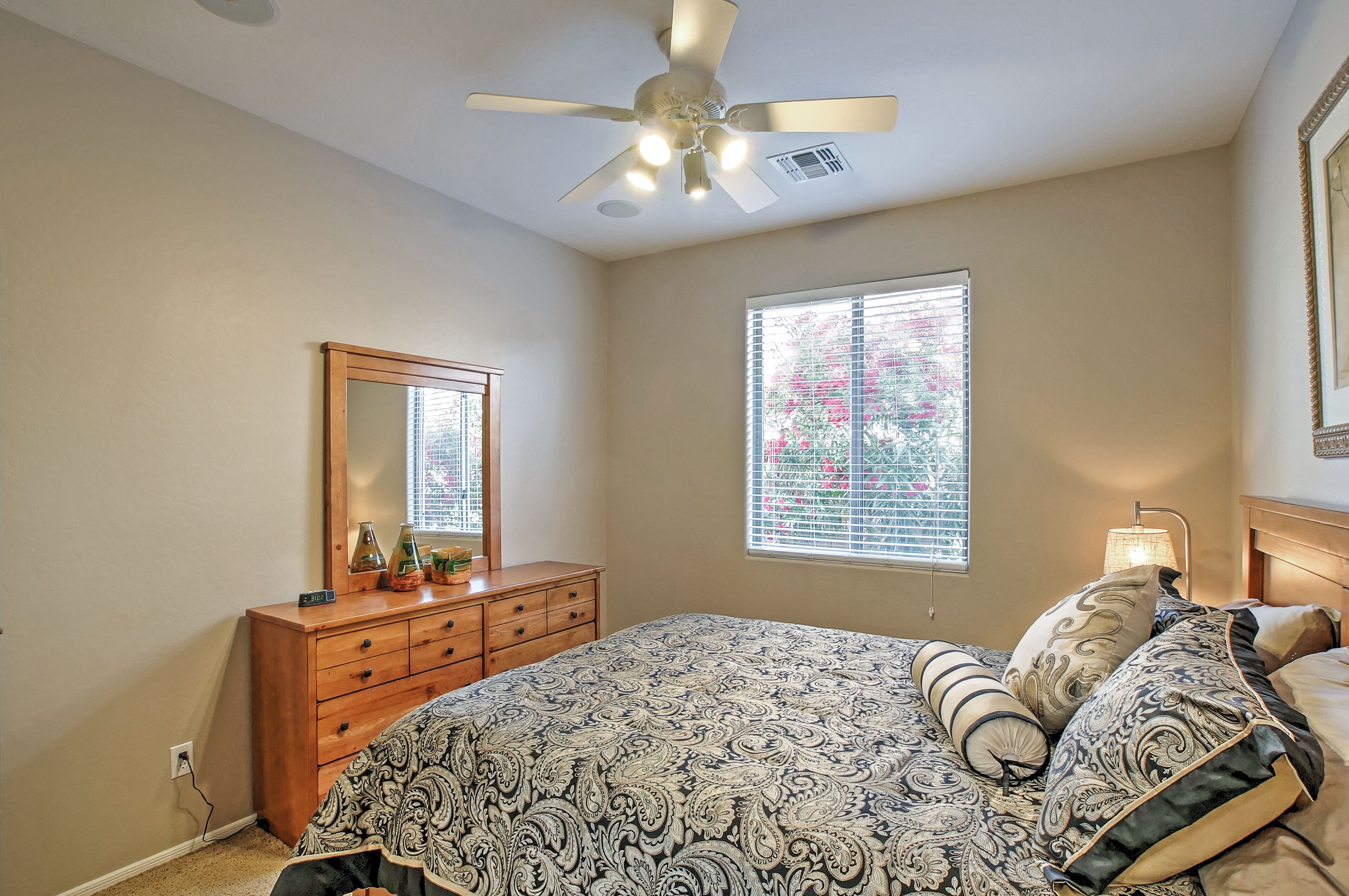Un dormitorio con cama, cómoda, espejo, ventana, ventilador de techo y lámpara.