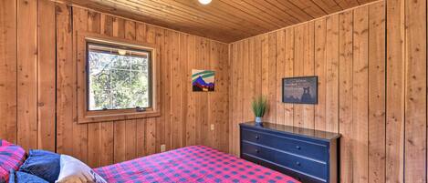 Una habitación con paneles de madera, una cama, un aparador, una ventana y un cuadro en la pared.
