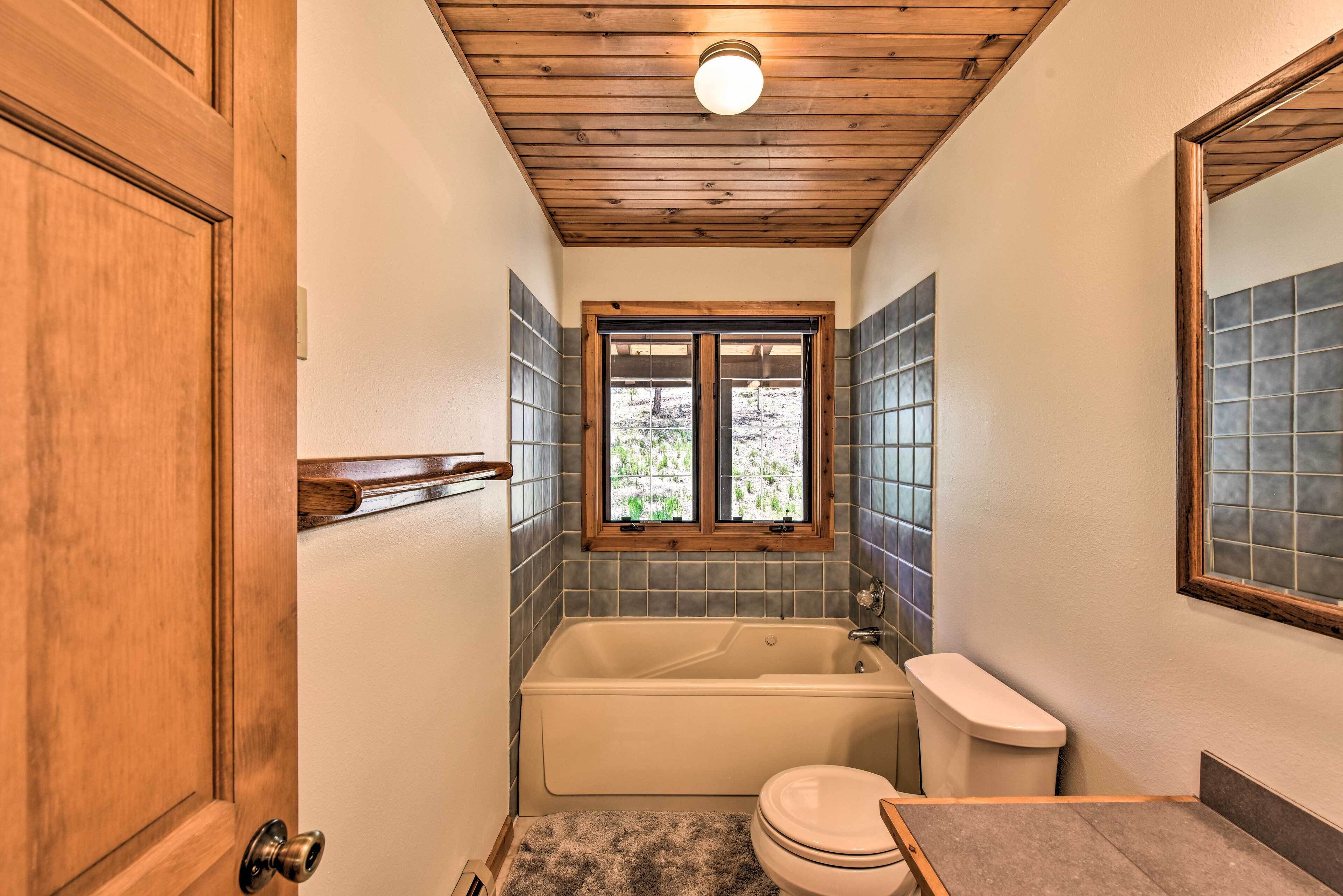 Un baño con techo de madera, una bañera, un inodoro y una ventana con vista a la vegetación.
