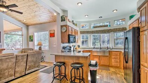 Une cuisine spacieuse avec des meubles en bois, un grand îlot central doté de tabourets, un réfrigérateur et un ventilateur de plafond.