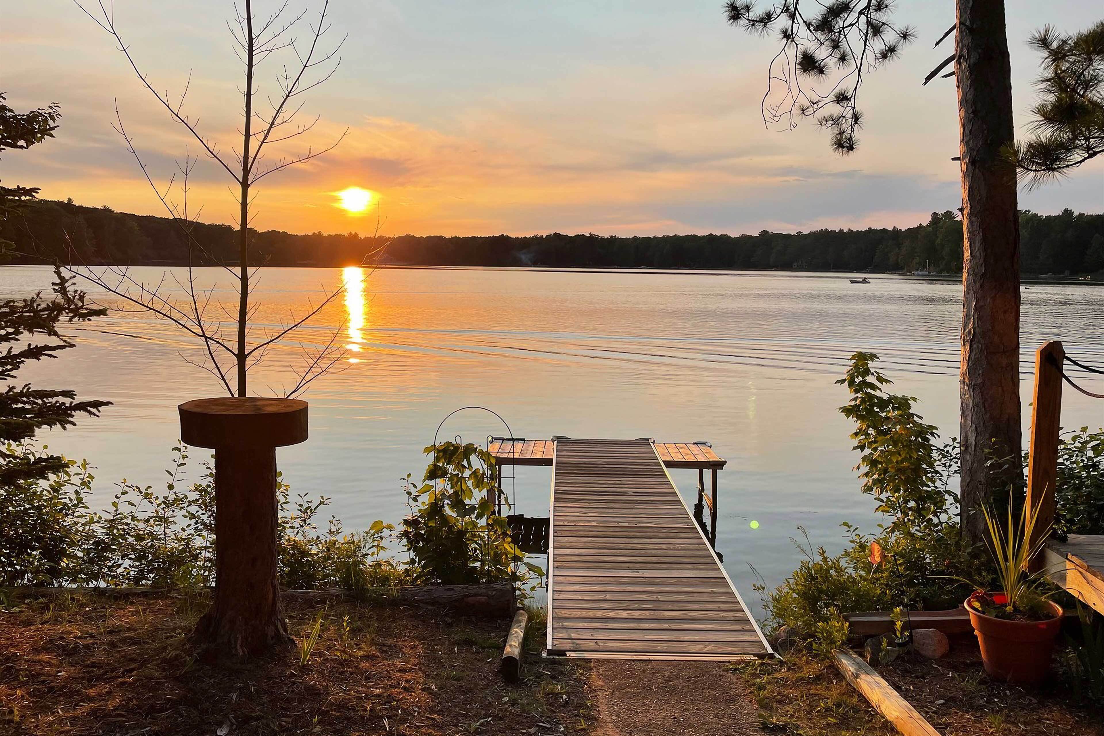 A wooden dock extending into calm water with a sunset in the background.