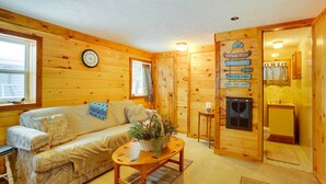 A cozy cabin interior with a wooden floor, a sofa, a coffee table with a plant, a clock, and a sign with 'COTTAGE RULES'. - Pine Ridge Resort Cabin on Bass Lake w/ Dock! (Interlochen)
