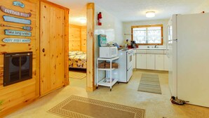A cozy cabin interior with a wooden exterior, a kitchenette with a refrigerator, microwave, and sink, and a bed with a patterned blanket. - Pine Ridge Resort Cabin on Bass Lake w/ Dock! (Interlochen)