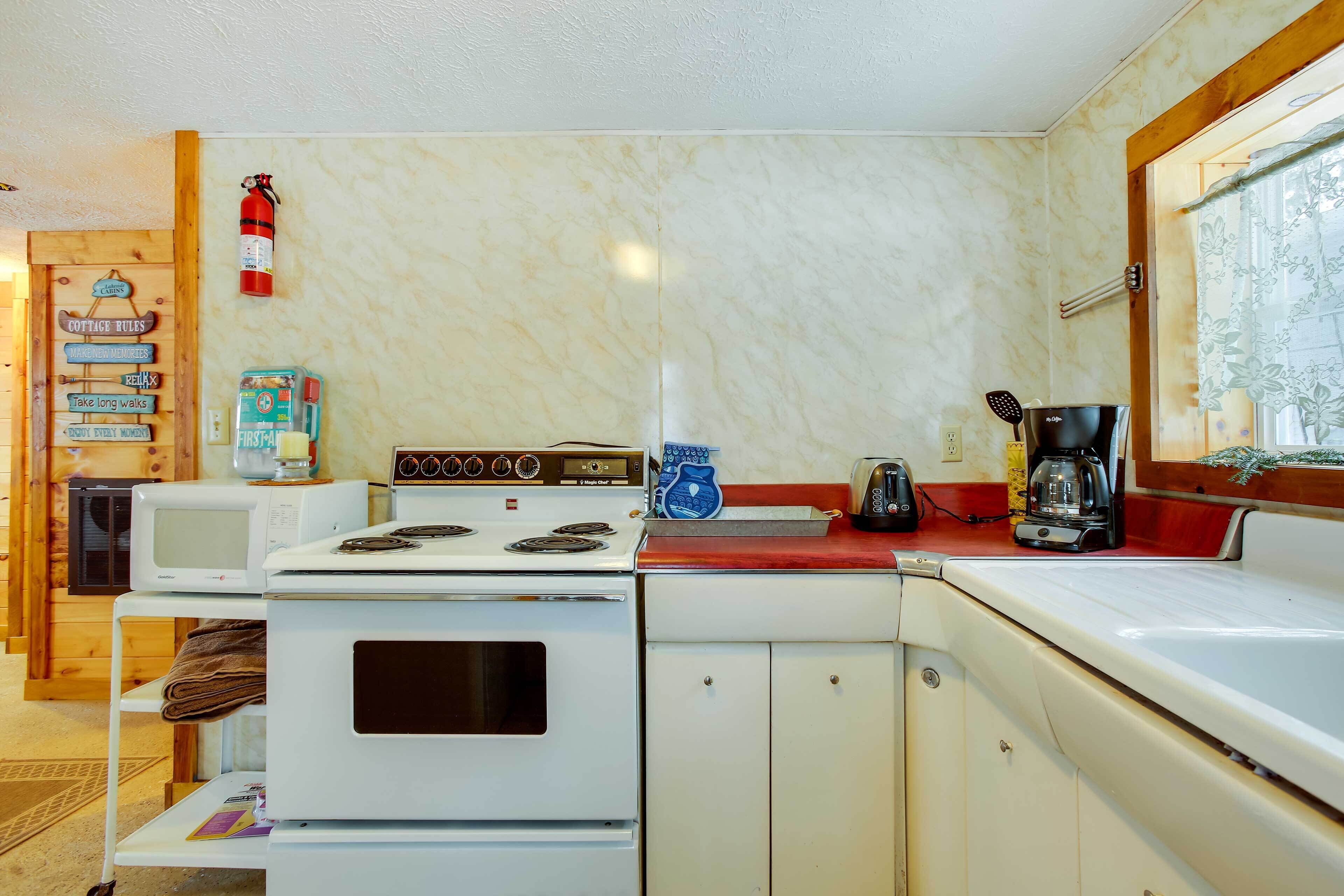 Cocina compacta con estufa, microondas y tostadora. Hay un extintor en la pared y un letrero de madera con normas.