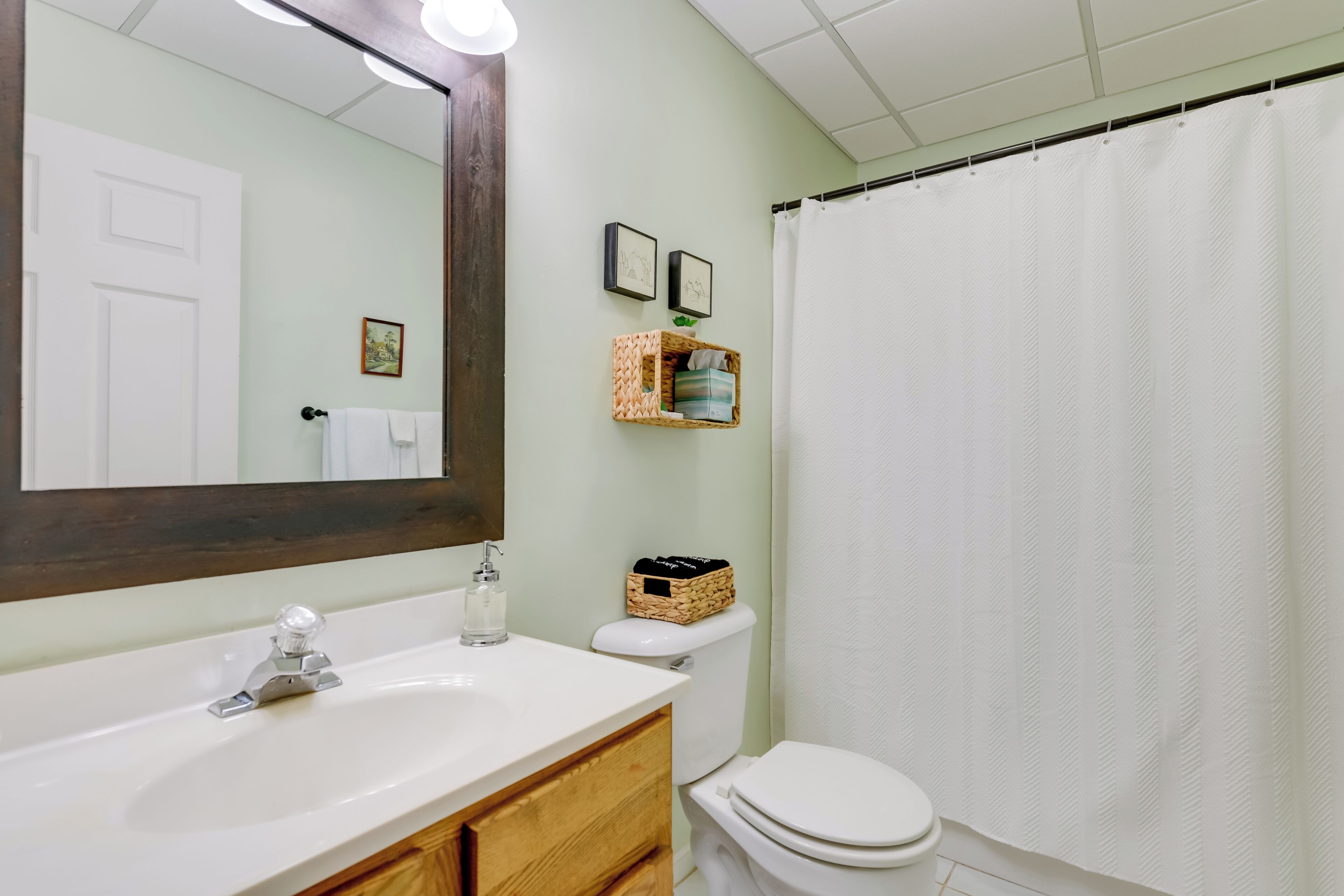 A bathroom with a white sink, a mirror, a toilet, and a shower curtain.