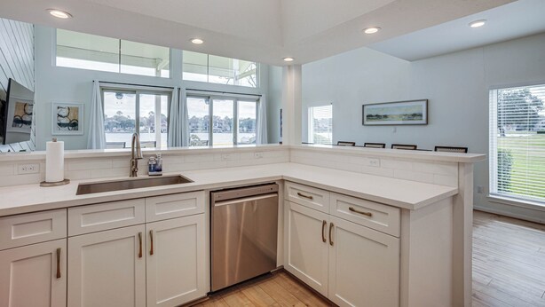 A modern kitchen with white cabinetry, a stainless steel dishwasher, and large windows offering views of the city. - Gorgeous Lakefront Townhome w/ Pool Access & Views (Montgomery)