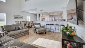 A spacious living room with a high ceiling, a modern kitchen, and a dining area with bar stools. - Gorgeous Lakefront Townhome w/ Pool Access & Views (Montgomery)