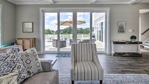 A spacious living room with a large sliding glass door leading to a deck, a striped armchair, and a rustic console table.