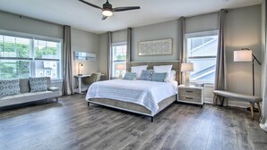 A spacious bedroom with a large bed, a bench, a desk, and a ceiling fan.