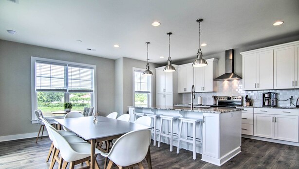 A modern kitchen with white cabinets, a central island with bar stools, pendant lighting, and a large window providing natural light.