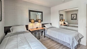 A hotel room with two beds, a desk with lamps, a mirror, and a framed picture on the wall.