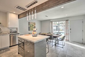 Une cuisine moderne dotée d’un îlot central, d’appareils électroménagers en acier inoxydable et de luminaires suspendus.